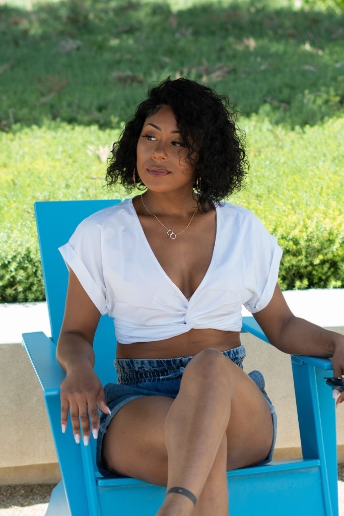 BLACK WOMEN sitting outside on blue chair wearing a White Front Tie Crop Top and high waist denim shorts